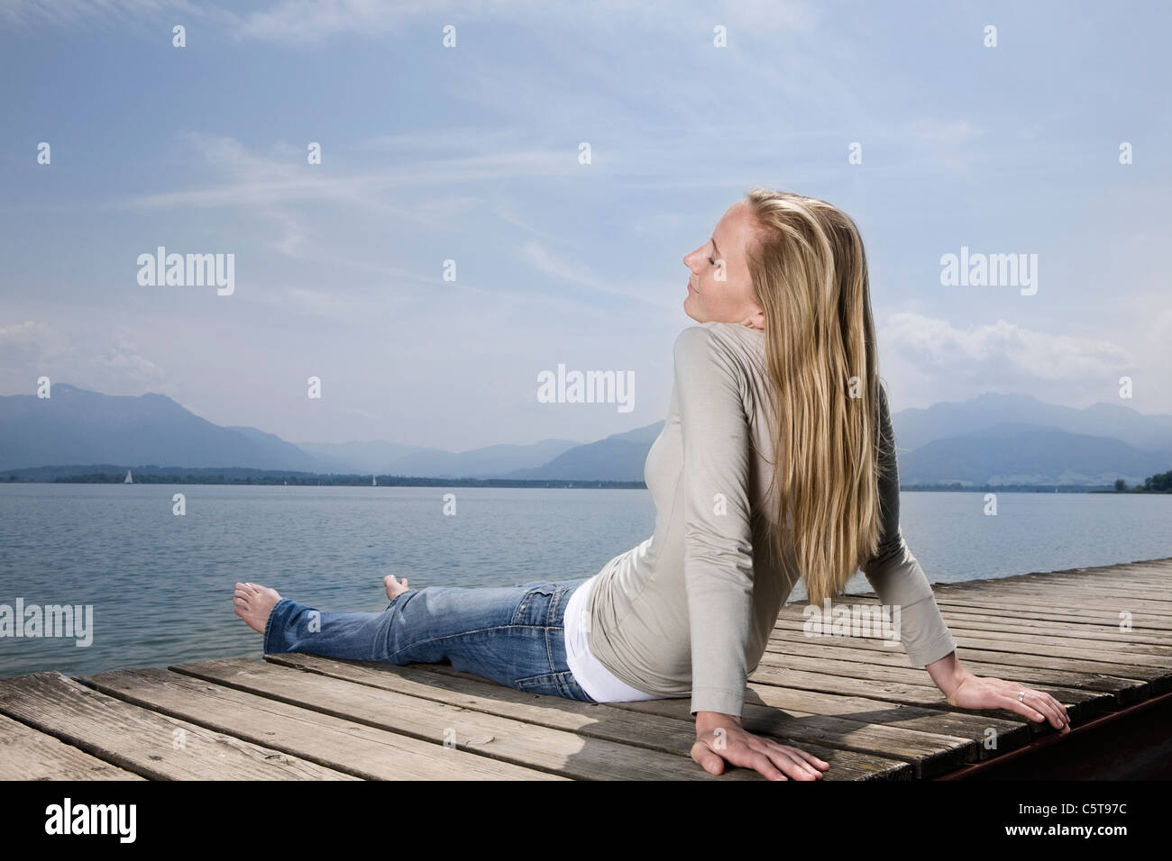 Germany, Chiemsee, Woman sitting on jetty, eyes closed Stock Photo
