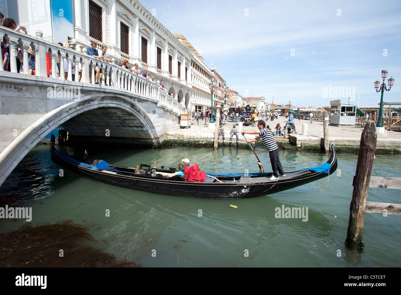 Venice Italy Grand Canal and famous Rialto Bridge. Gondolas going underneath and  tourists on bridge. Restaurants and businesses Stock Photo