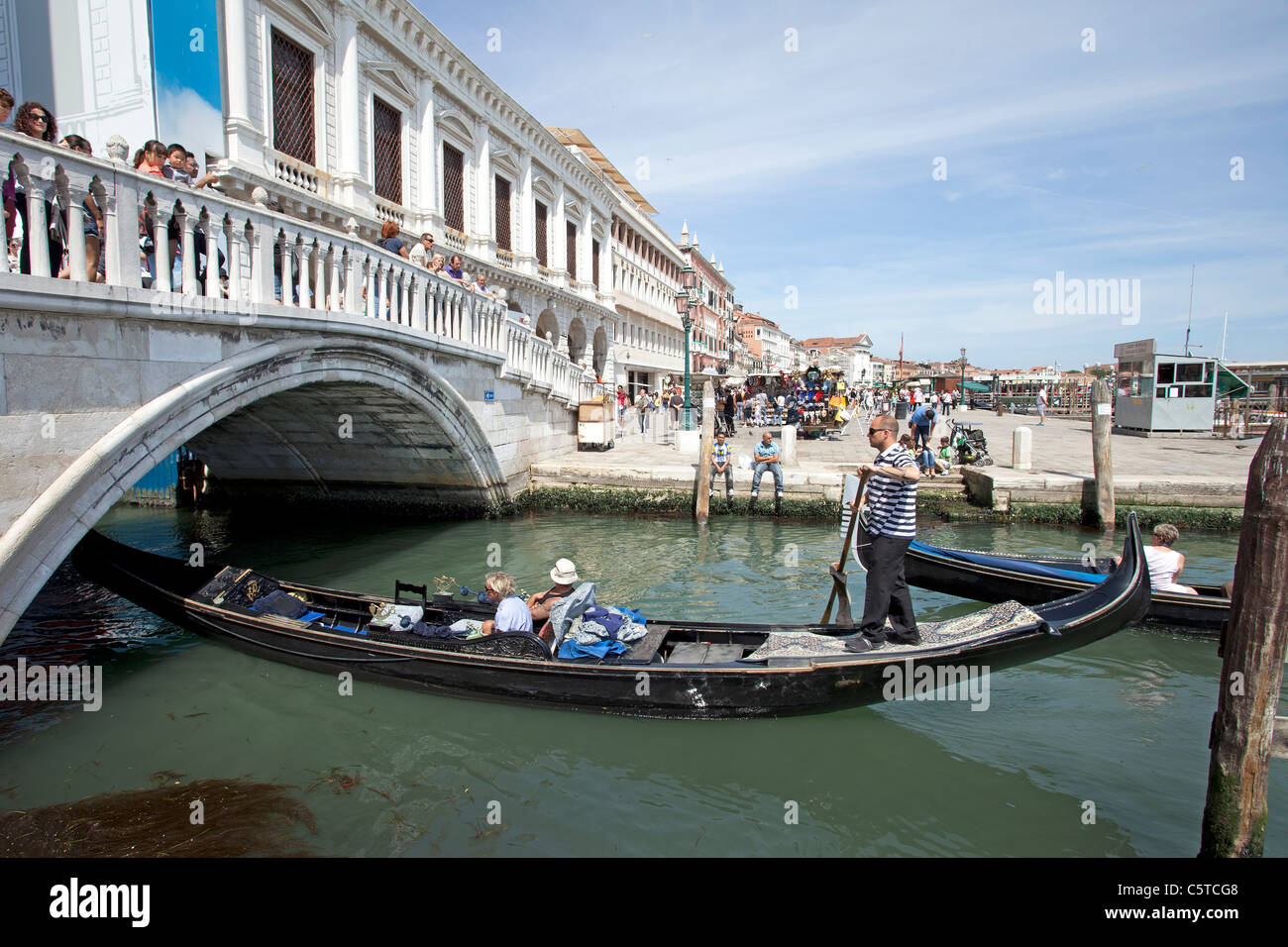 Venice Italy Grand Canal and famous Rialto Bridge. Gondolas going underneath and  tourists on bridge. Restaurants and businesses Stock Photo