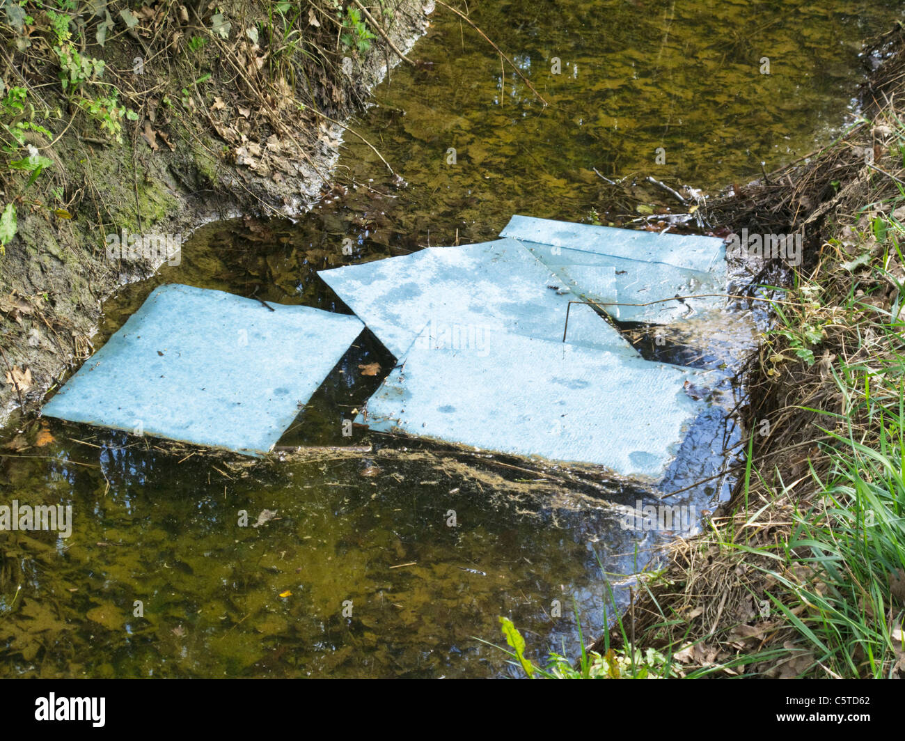 Absorbent spillage pads floating on stream cleaning up diesel spillage in water. Stock Photo