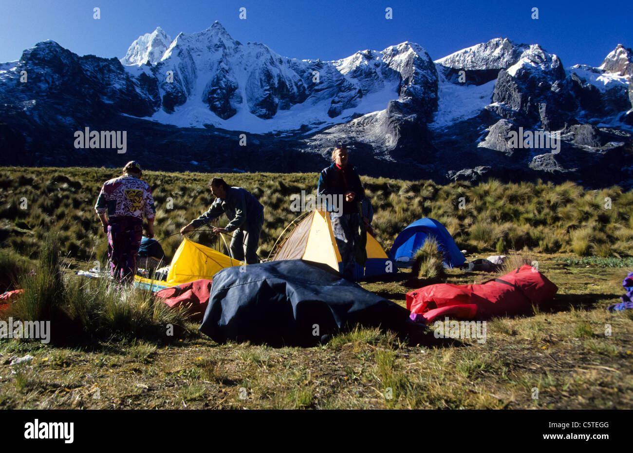 tourists and treckers putting up tents in front of snow capped Cordillera Blanca mountains Stock Photo