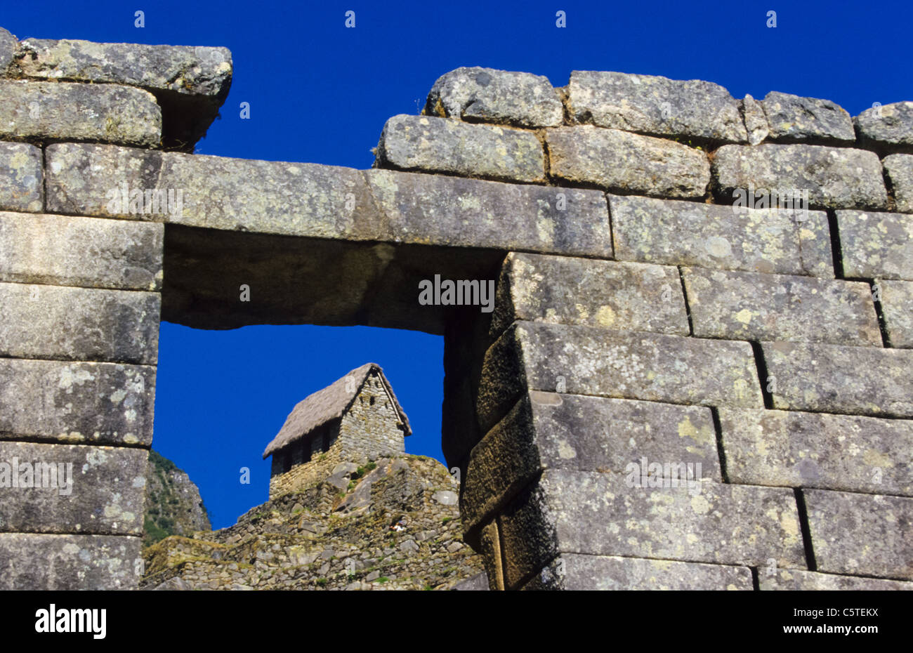 Complete Inka house with roof seen through gate in Stone wall at Machu Picchu in Peru Stock Photo