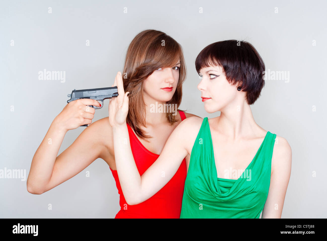 two young female friends playing with a gun - isolated on gray Stock Photo