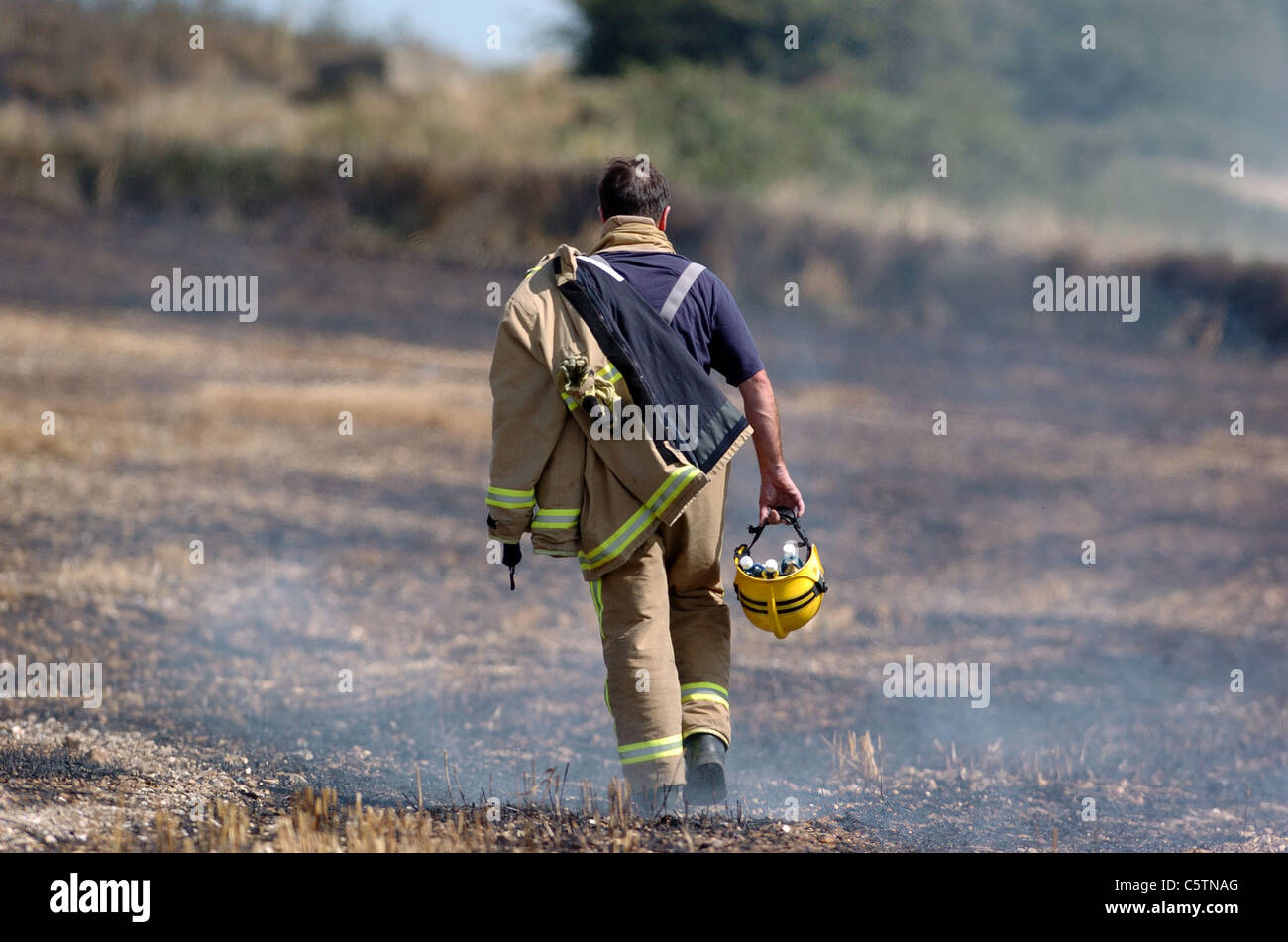 Members of the Fire Brigade make their way back across charred fields after they had put out the field fires nr Brighton UK Stock Photo