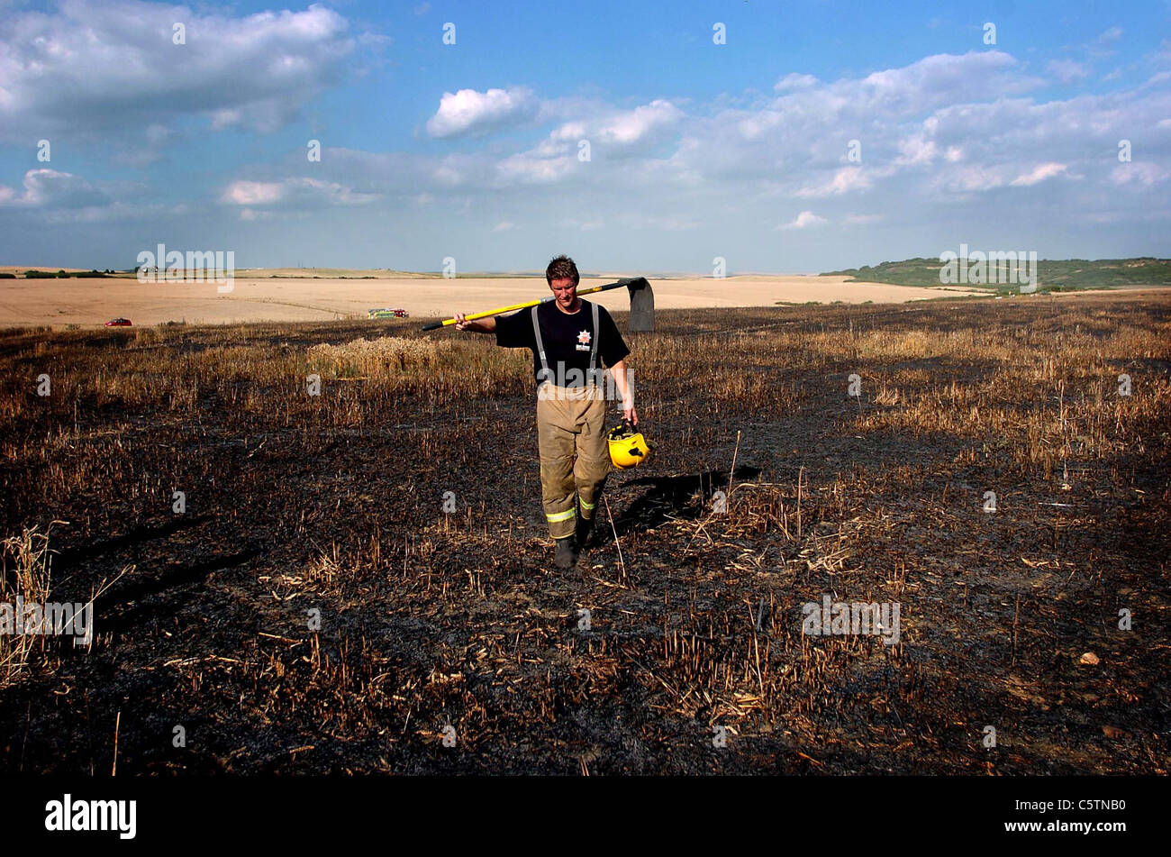 Members of the Fire Brigade make their way back across charred fields after they had put out the field fires nr Brighton UK Stock Photo