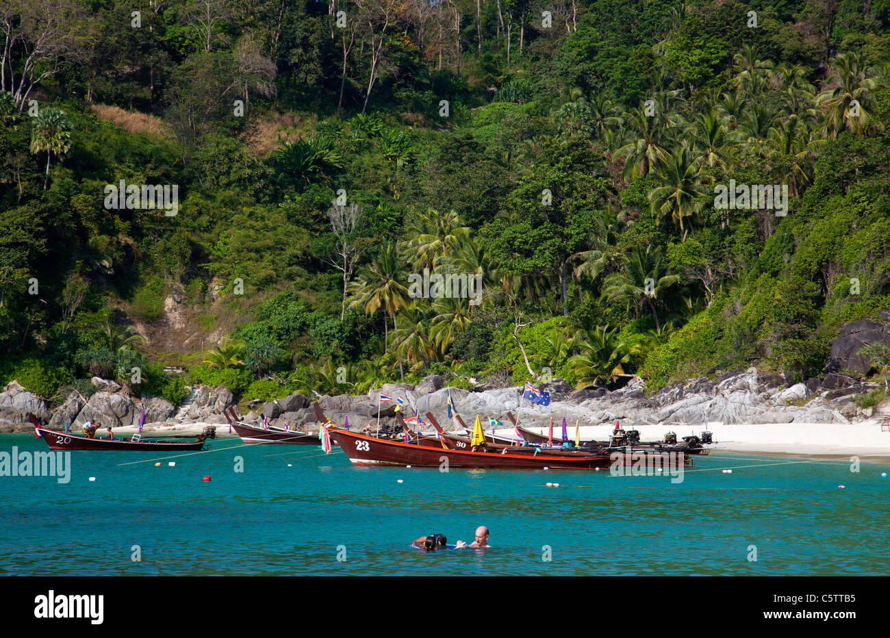 Longtail Boats anchored along Freedom Beach and people swimming in the Andaman Sea . Stock Photo