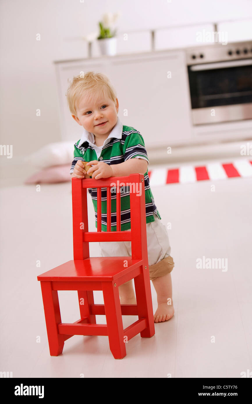 Baby boy (1-2) standing behind red chair Stock Photo - Alamy