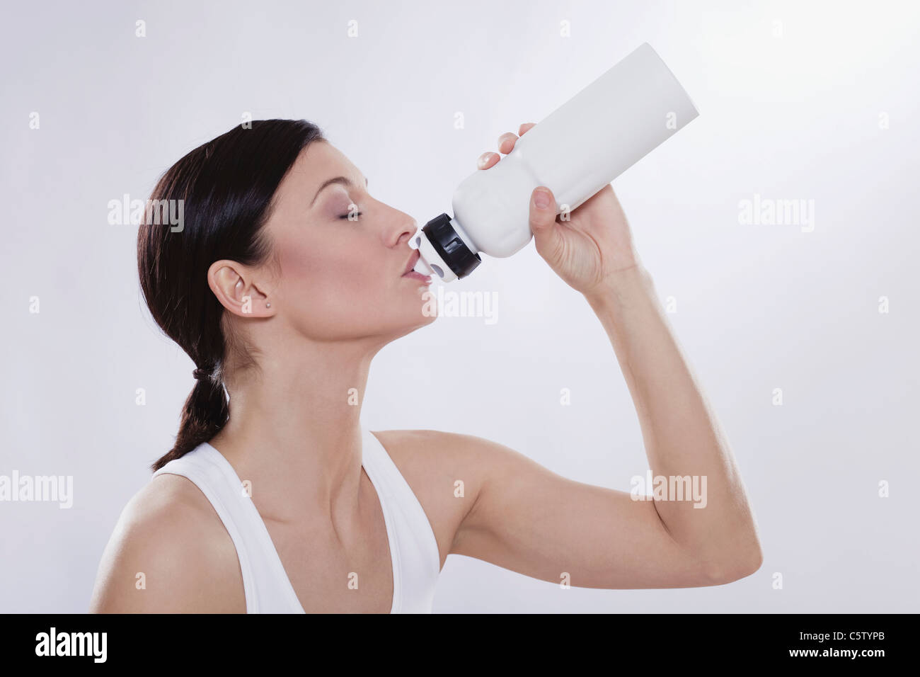Mid adult woman drinking from water bottle against white background Stock Photo