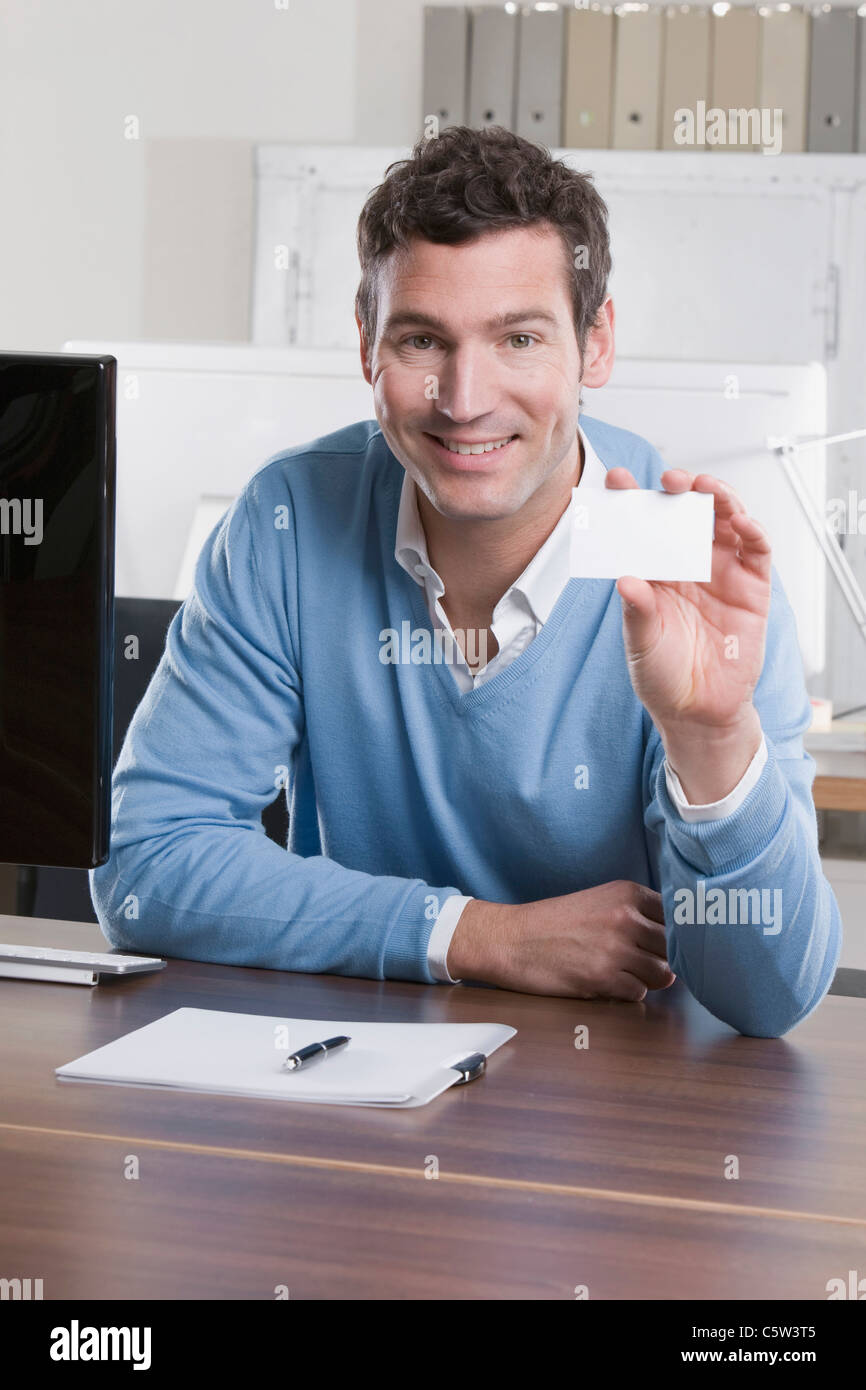 Germany, Munich, business man in office holding business card, smiling
