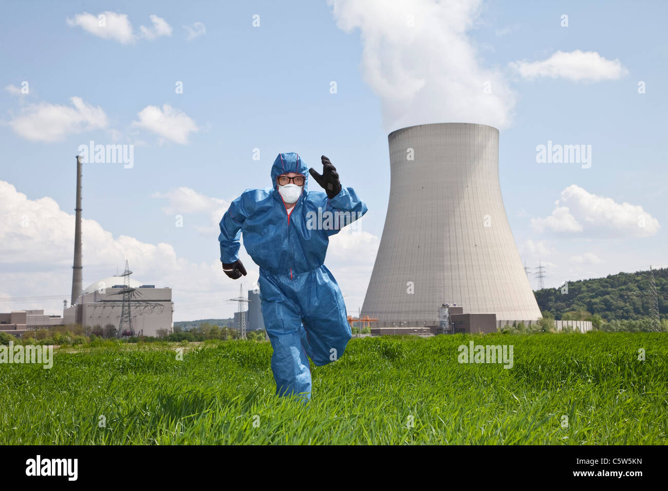 Germany, Bavaria, Unterahrain, Man with protective workwear running in field at AKW Isar Stock Photo