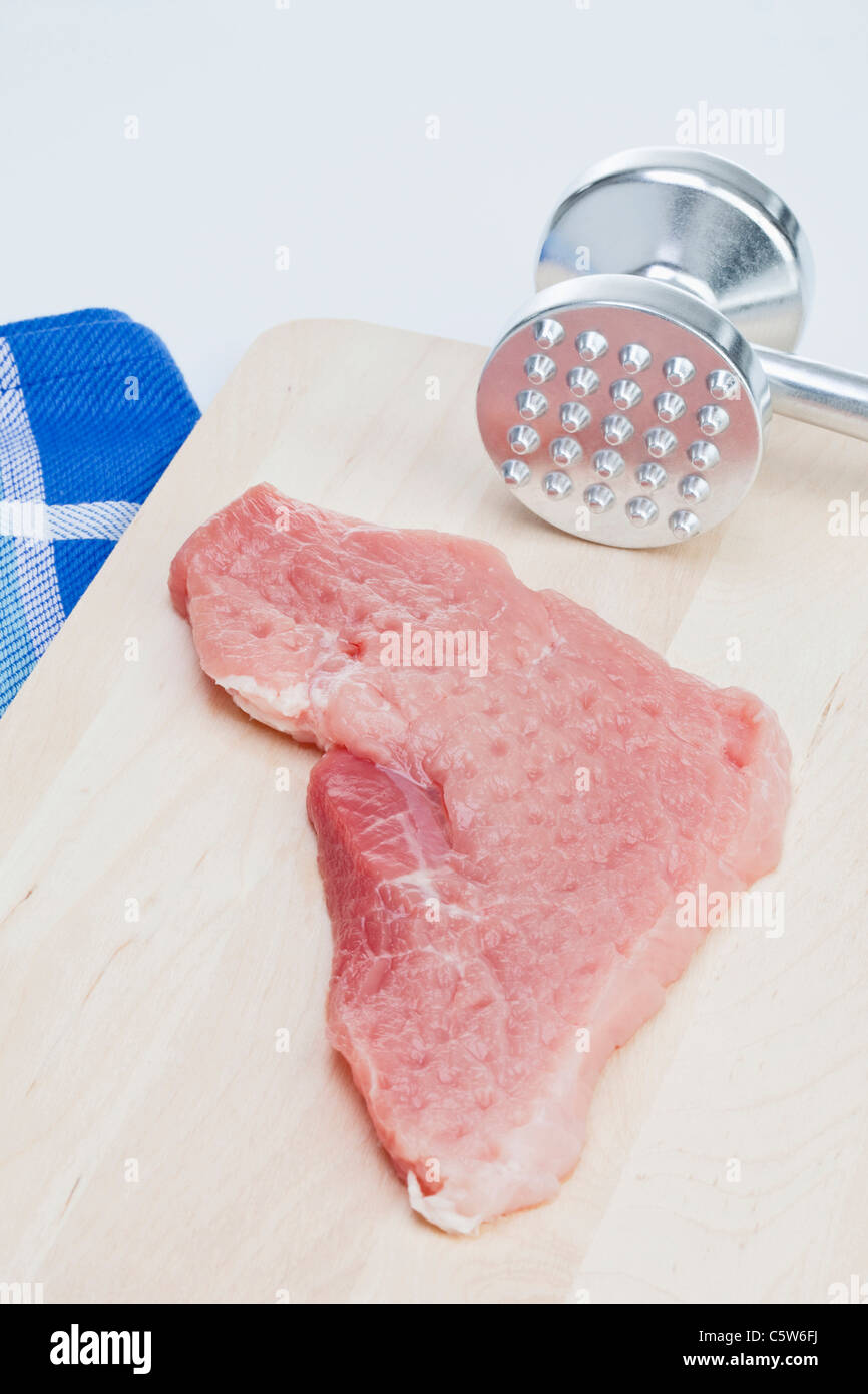Raw cutlet and meat tenderizer on chopping board, elevated view Stock Photo