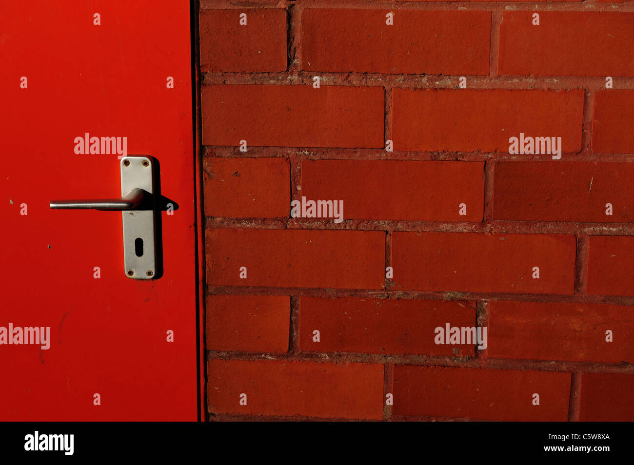 fire engine red door in redbrick wall aluminium door handle Stock Photo