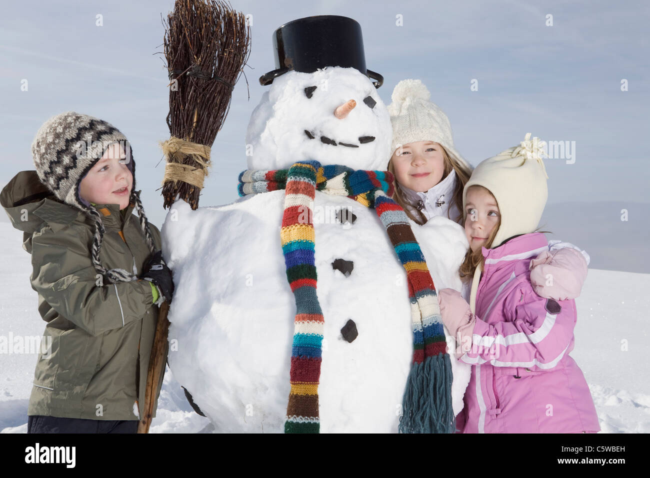 Germany, Bavaria, Munich, Children (4-5) (8-9) standing next to snowman, portrait Stock Photo