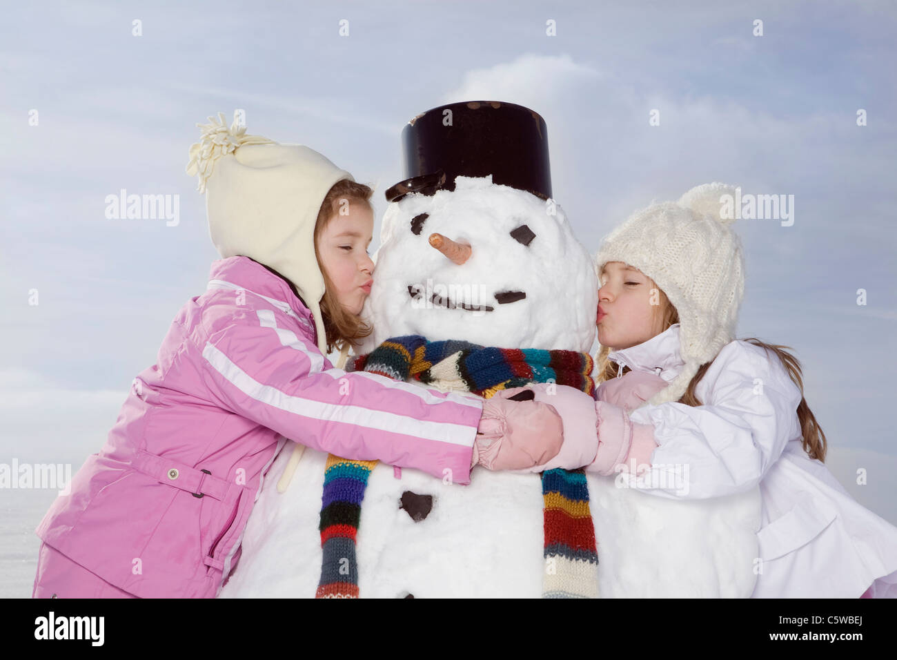 Germany, Bavaria, Munich, Two girls (4-5) (8-9) kissing snowman, eyes closed, portrait Stock Photo