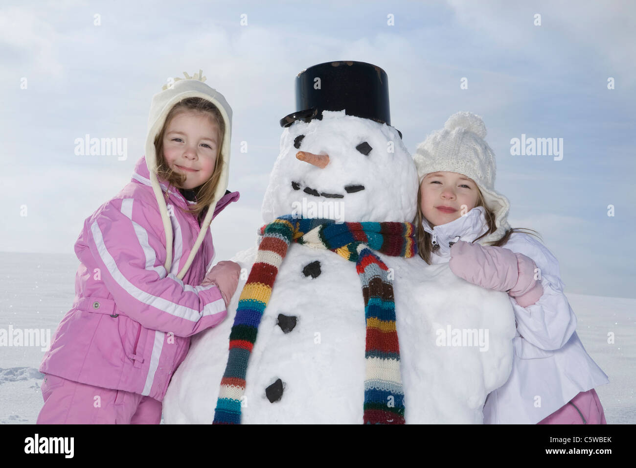 Germany, Bavaria, Munich, Two girls (4-5) (8-9) standing next to  snowman, smiling, portrait Stock Photo