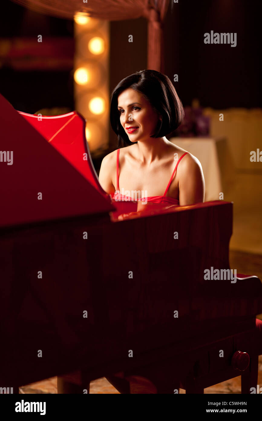 beautiful brunette woman in red dress playing piano Stock Photo - Alamy