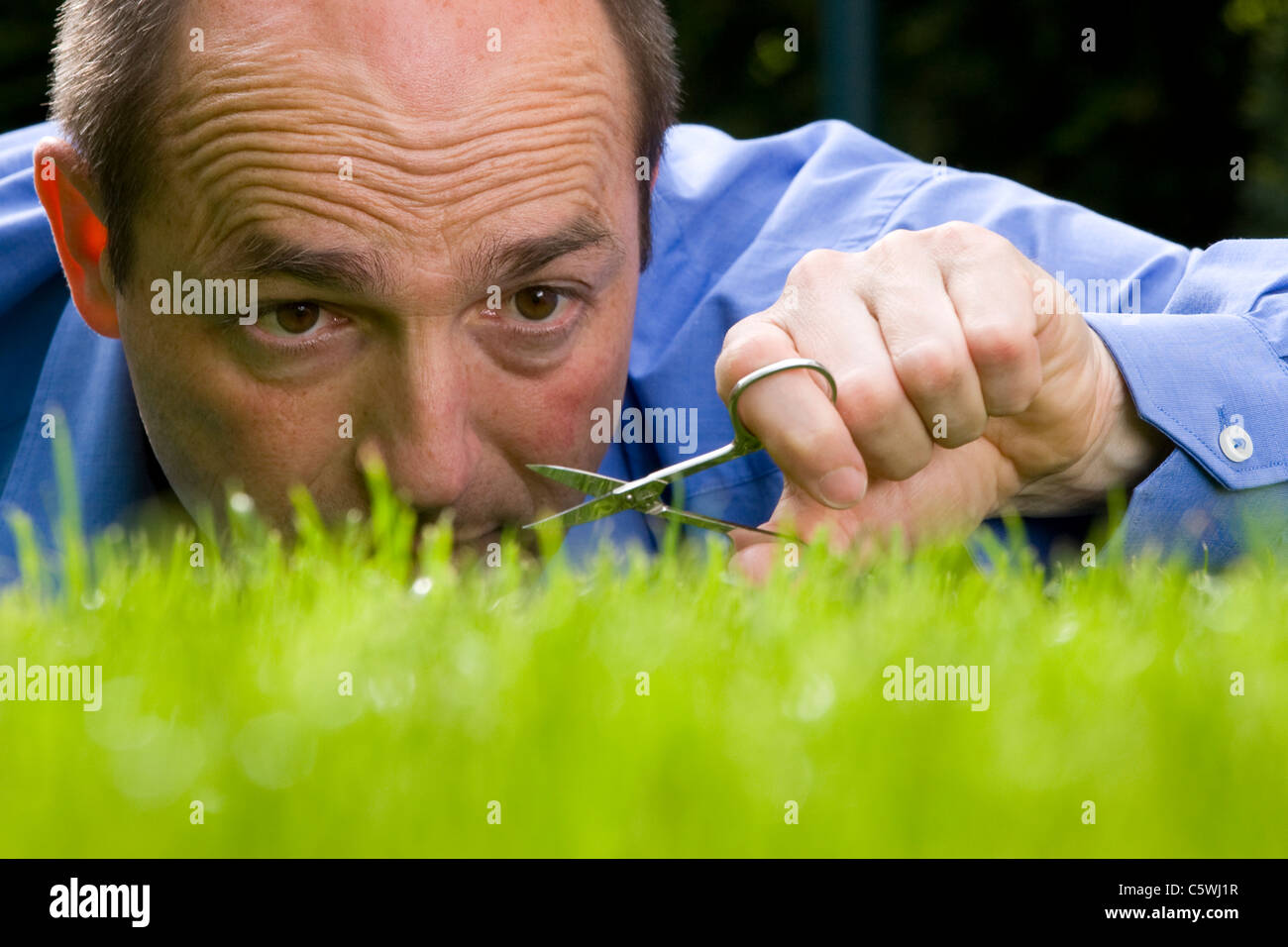 Germany, Baden-WÃ¼rttemberg, Stuttgart, Man cutting grass with scissors Stock Photo