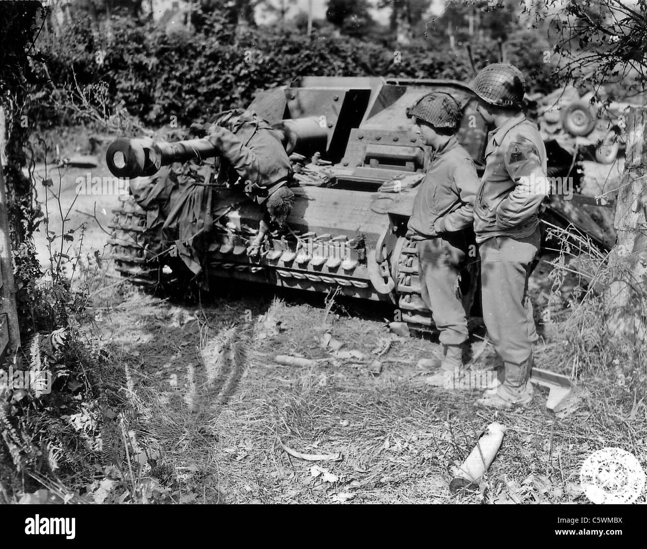 NORMANDY INVASION 1944 Two US soldiers from 3rd Armoured Division with knocked out Sturmgeschutz and dead German crew member Stock Photo