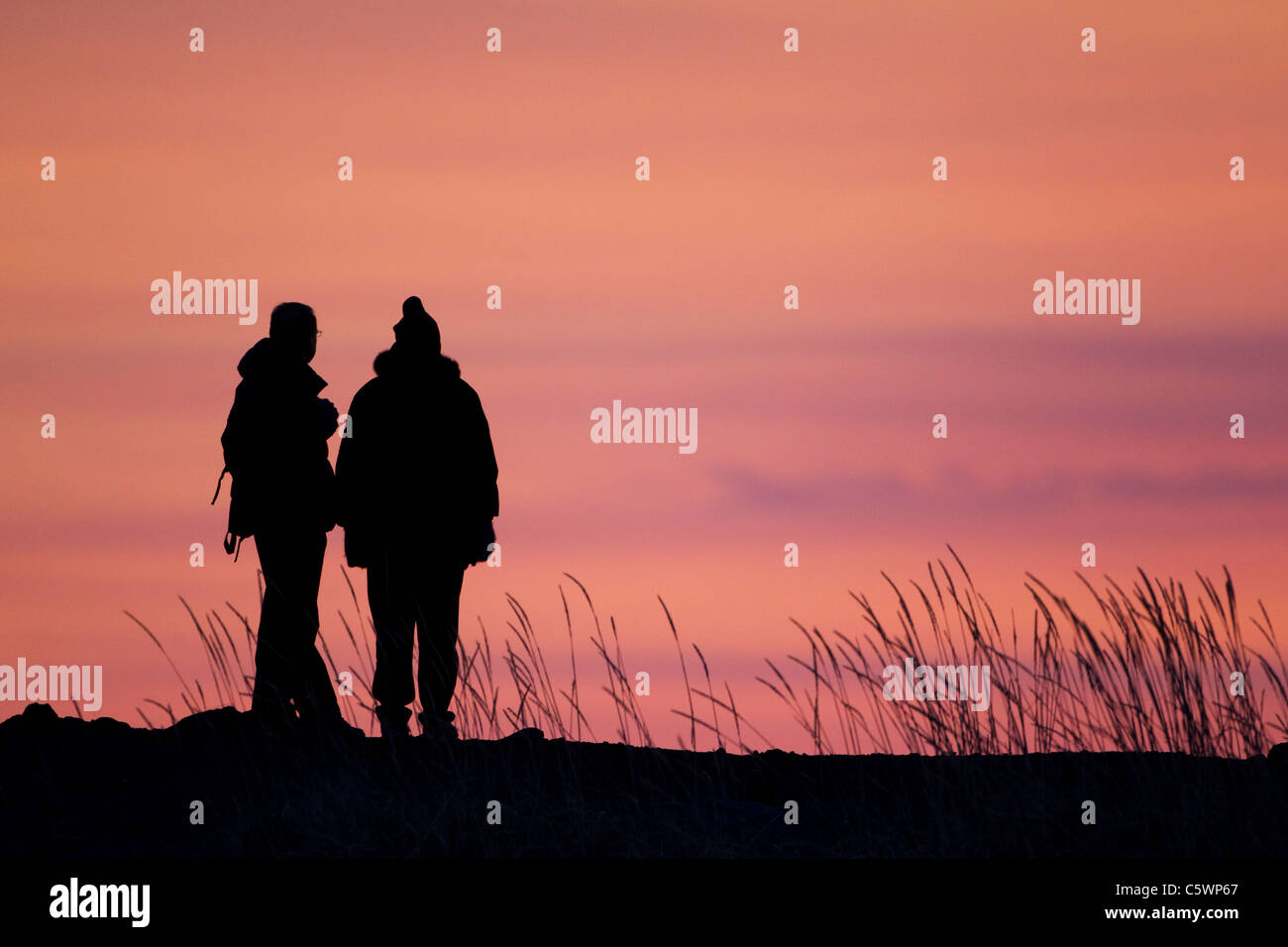 Couple silhouetted at sunset on coastal dunes, Great Britain. Stock Photo