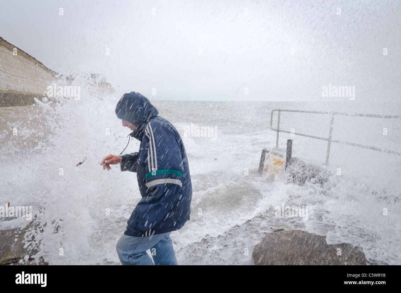 A man braves the stormy weather at Saltdean, East East Sussex, promenade, as waves hit the breakwater. Stock Photo