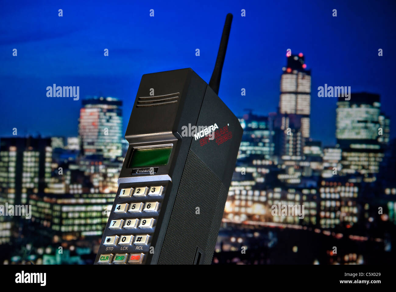 1980’s Mobile Cell Phone MOBIRA CITYMAN 1987 First generation early hand held mobile cell phone Mobira Cityman 1320 launched 1987, with 80’s contemporaneous 1987 London financial city skyline lit at dusk behind including Nat West Tower LONDON CITY Stock Photo
