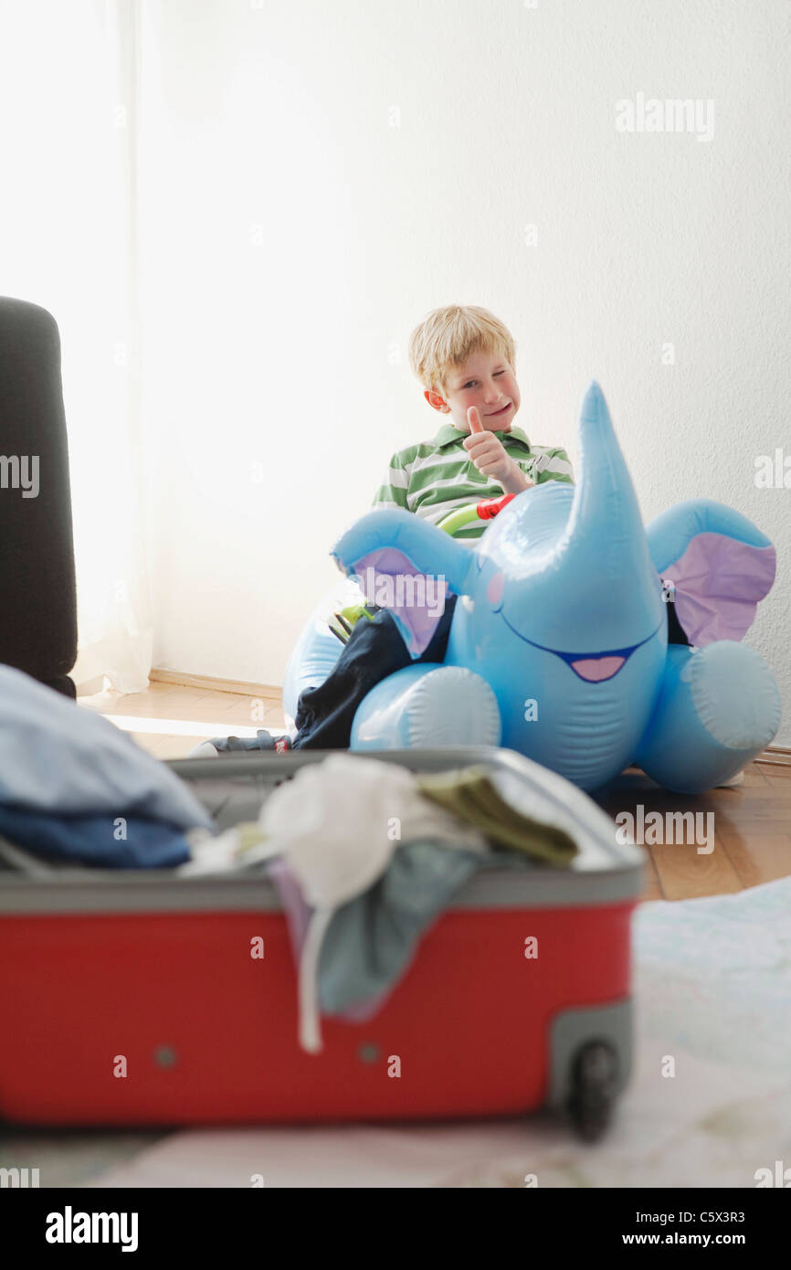 Germany, Leipzig, Boy (8-9) sitting on inflatable elephant, suitcase in foregroound Stock Photo