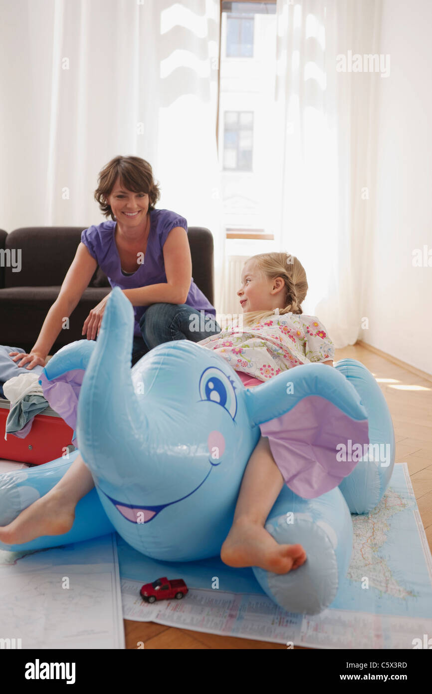 Germany, Leipzig, Girl (4-5) sitting on inflatable elephant, mother in background packing suitcase Stock Photo