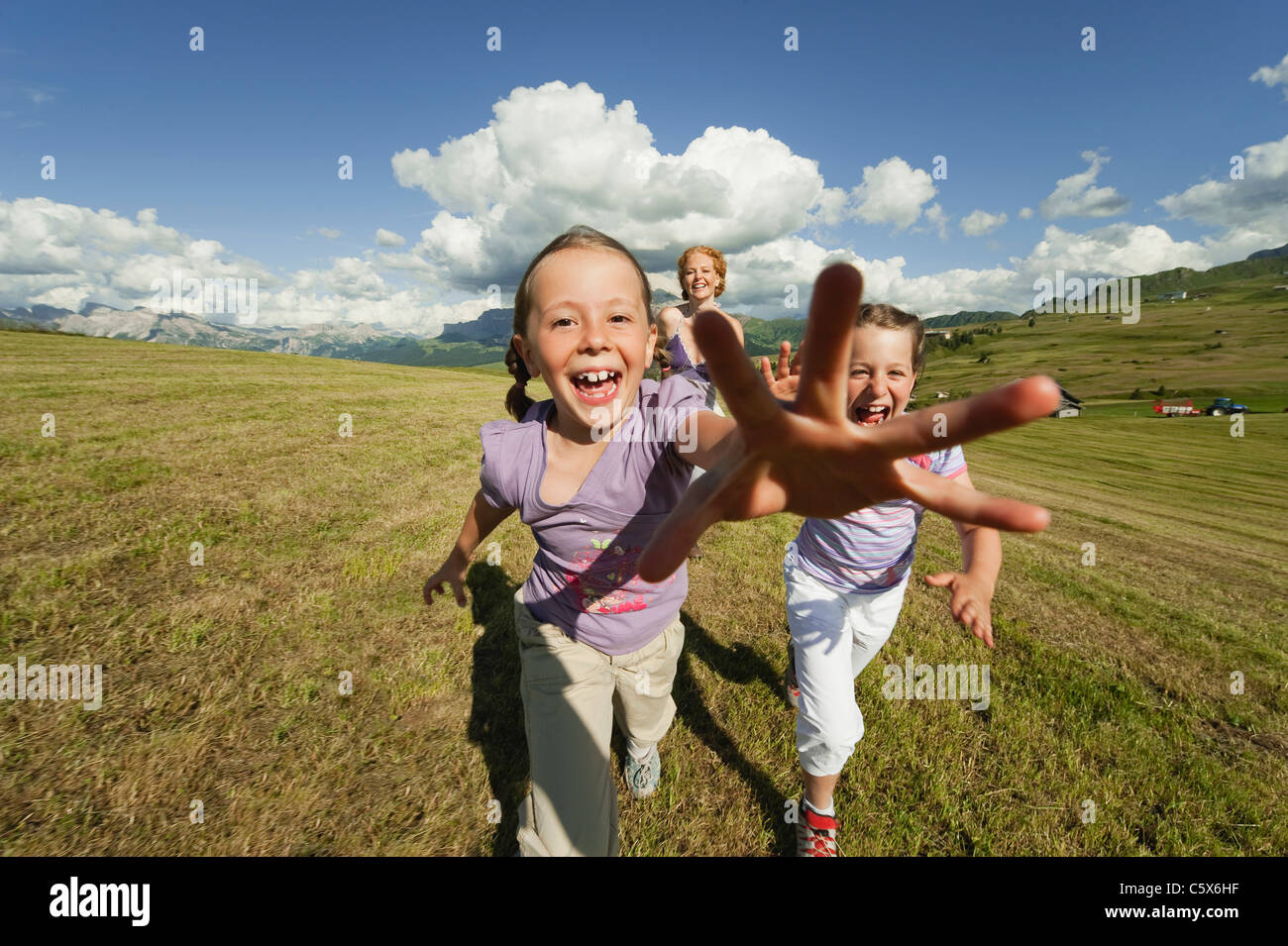 Italy, Seiseralm, Mother and daughters (6-7), (8-9) running in meadow, laughing, portrait Stock Photo