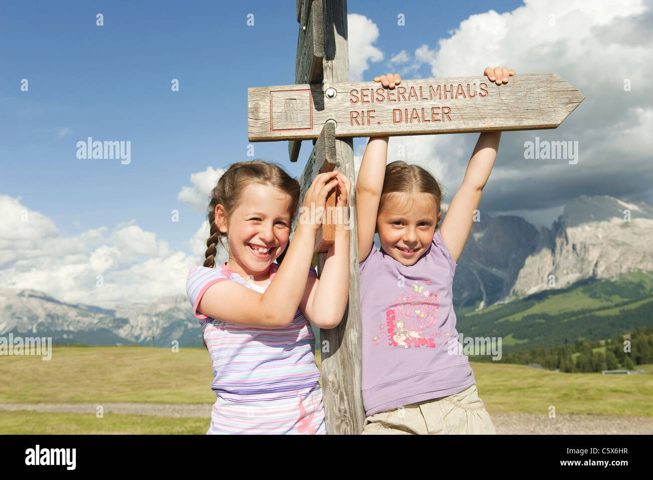 Italy, Seiseralm, Girls (6-7), (8-9) standing by sign post, smiling, portrait Stock Photo