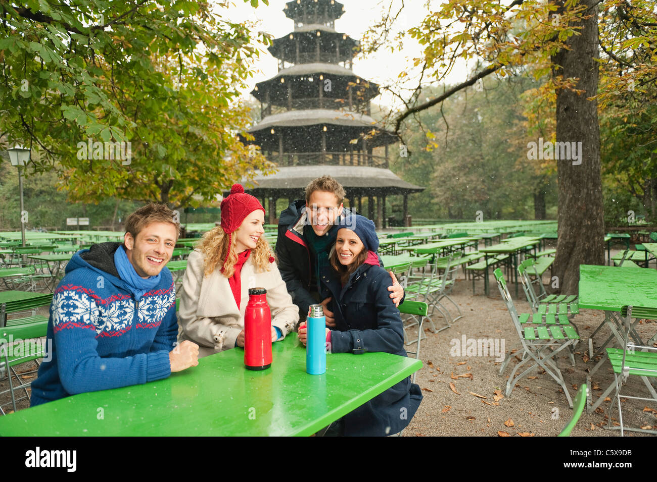 Germany, Bavaria, English Garden, Beer Garden, Four sitting in beergarden, Chinese tower in background Stock Photo