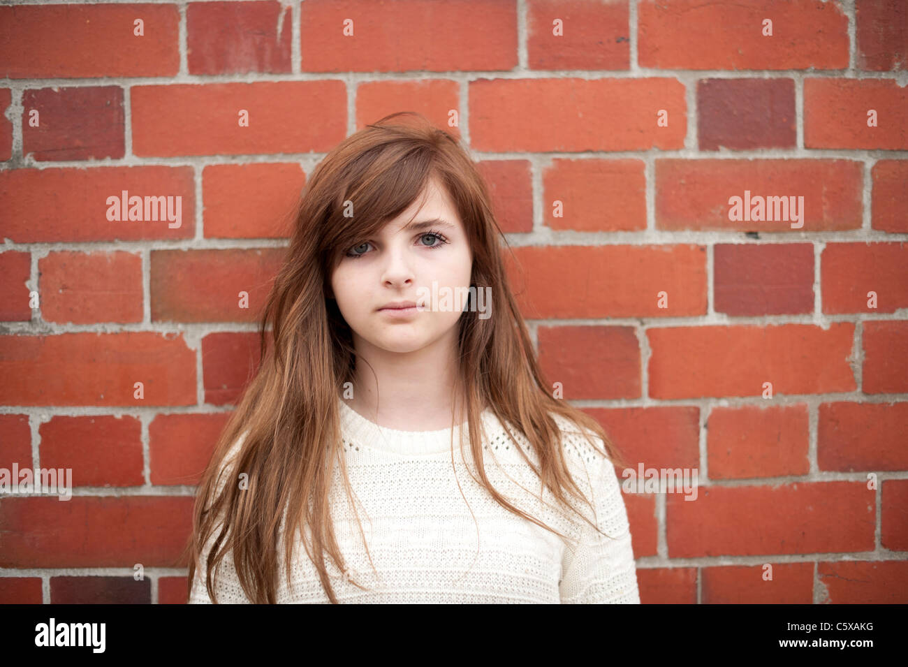 a twelve thirteen 12 13 year old teenage girl standing against a red brick wall Stock Photo