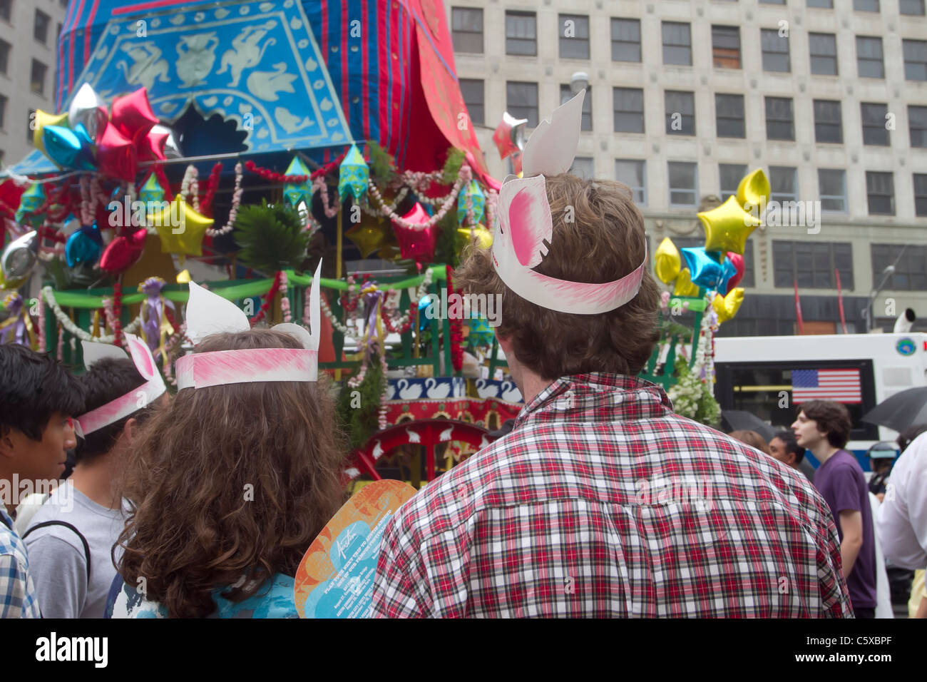 Spectators attending a barbecue festival in midtown Manhattan wearing paper pig ears watch the Hare Krishna parade Stock Photo