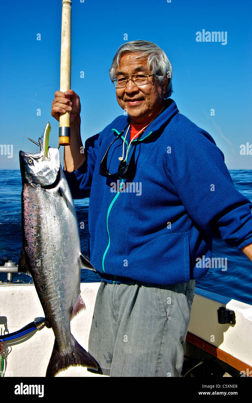 Asian male angler holding chinook salmon on gaff caught sport fishing Pacific Ocean west coast Vancouver Island Stock Photo