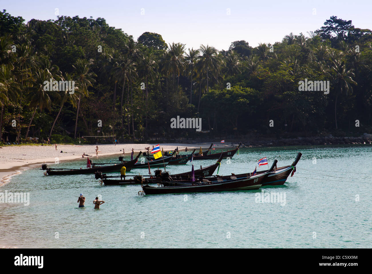 Holidaymakers swimming in clear water of the Andaman Sea at Freedom Beach and longtailboats anchored in bay. Stock Photo