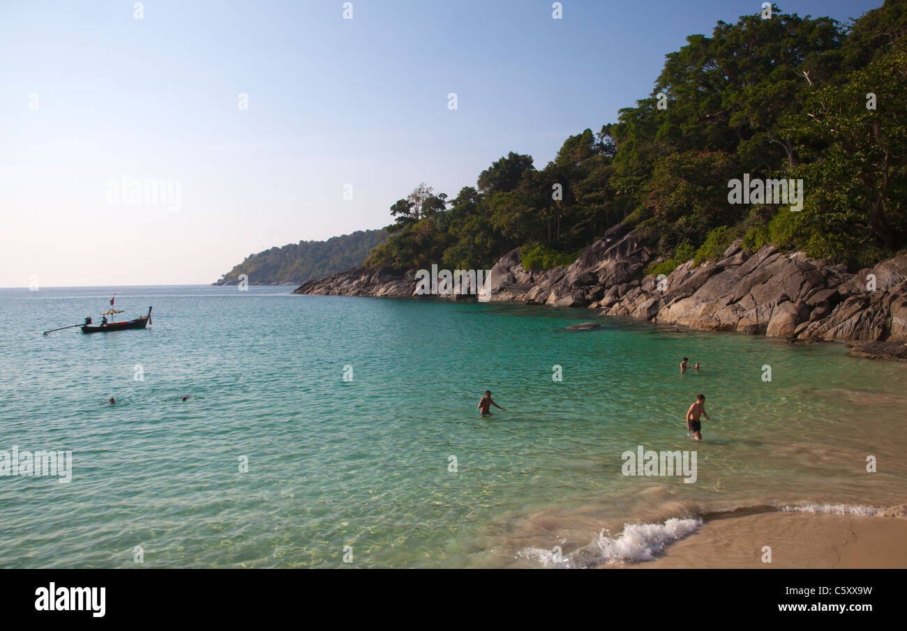 Holidaymakers swimming in clear water of the Andaman Sea at Freedom Beach and longtailboat anchored in bay. Stock Photo