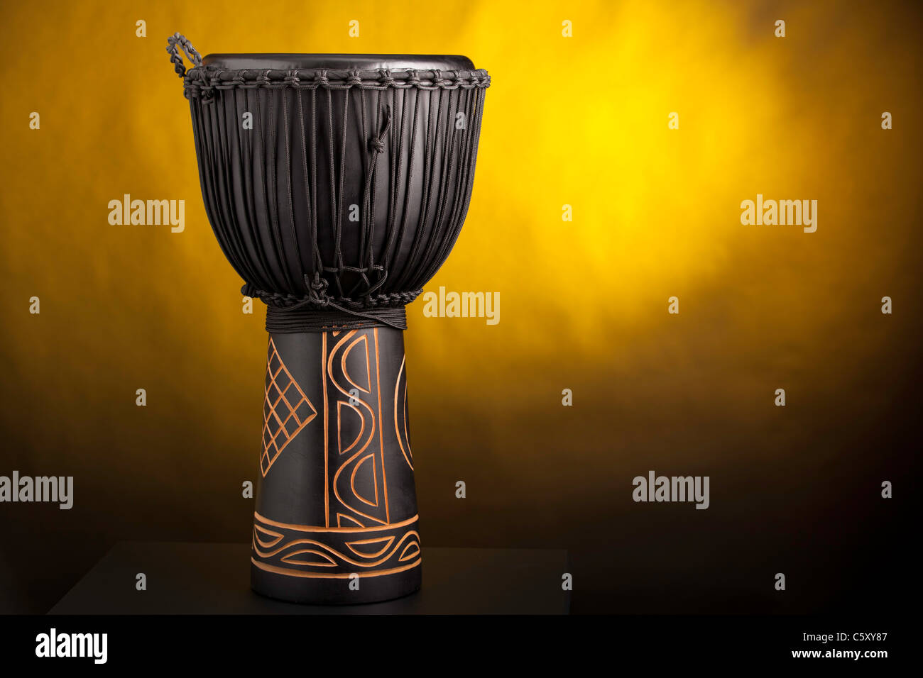 A black djembe conga drum isolated against a yellow spotlight