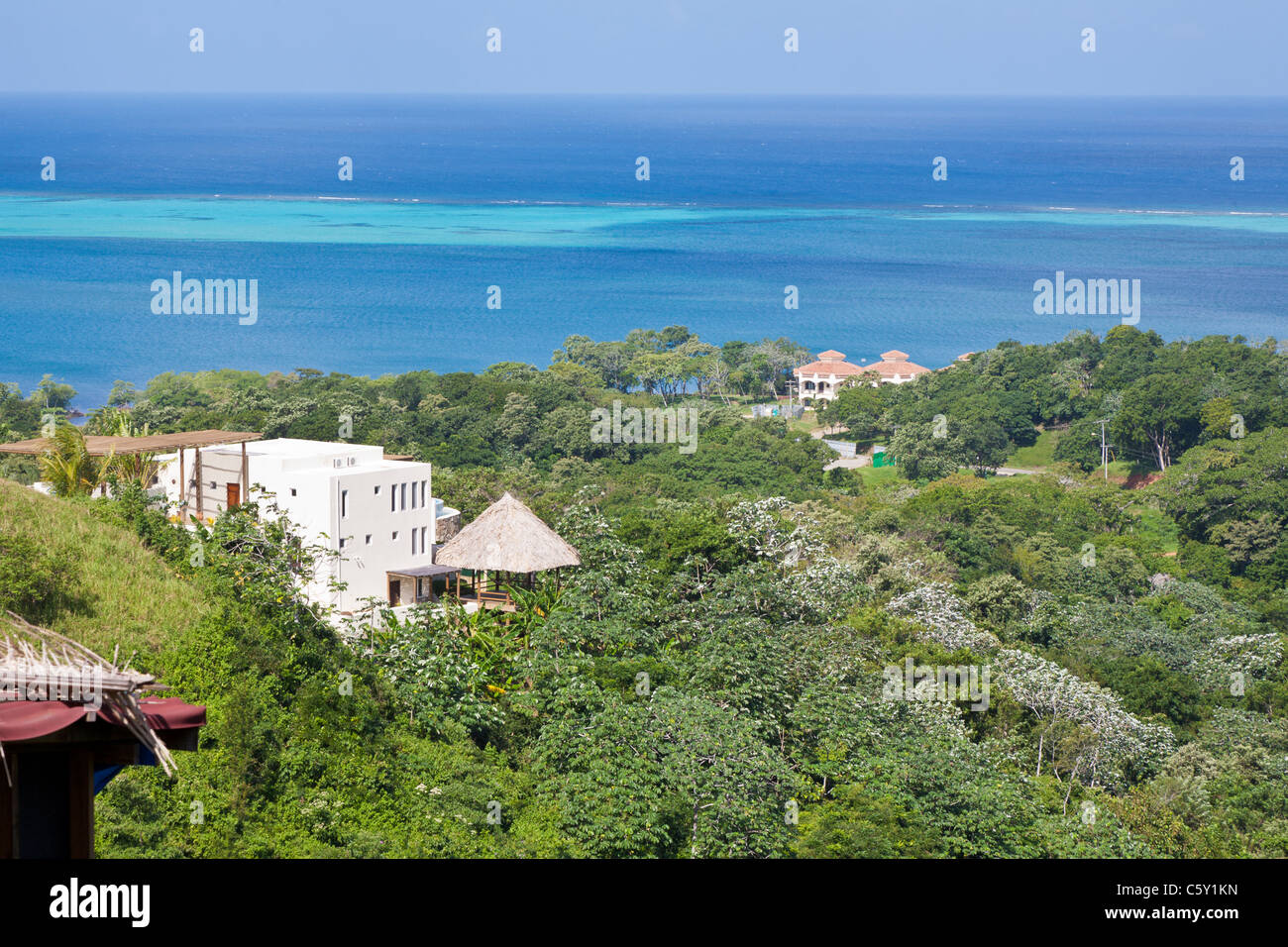Building with straw roof on green hillside overlooking the Caribbean Sea on the island of Roatan, in Honduras Stock Photo