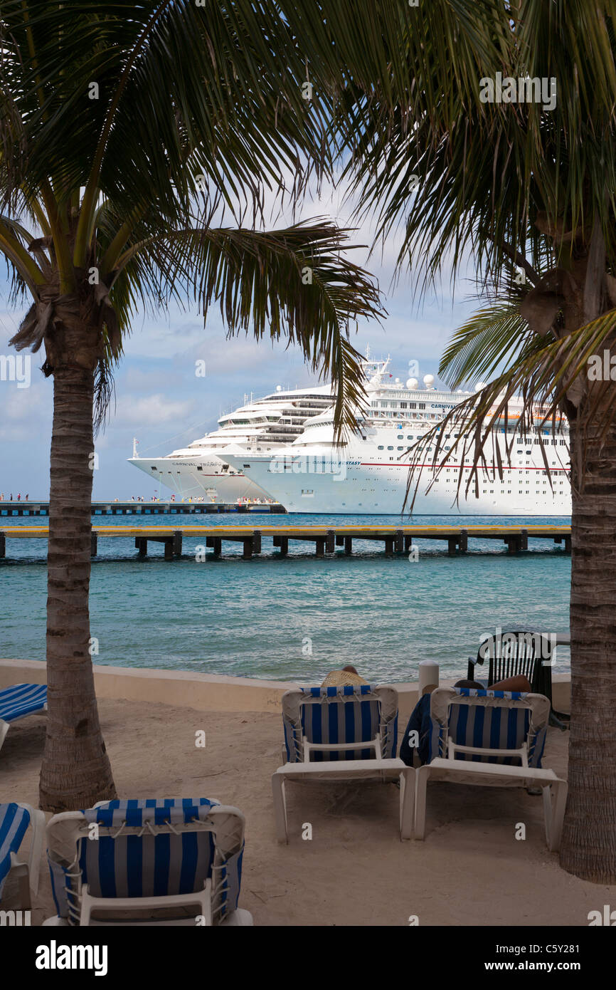 Carnival cruise ships Triumph and Ecstasy at pier are seen through palm trees at the port of Cozumel, Mexico in the Caribbean Stock Photo