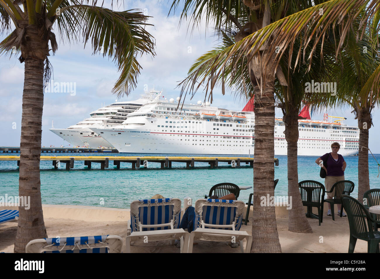 Carnival cruise ships Triumph and Ecstasy at pier are seen through palm trees at the port of Cozumel, Mexico in the Caribbean Stock Photo