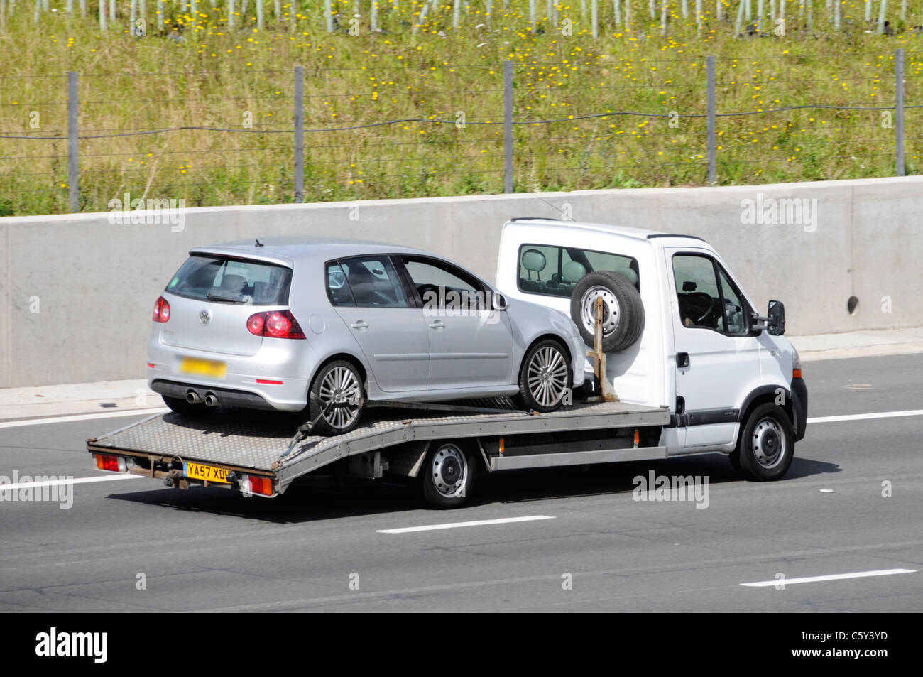 Loaded white unmarked transporter van truck a commercial vehicle transporting five door hatchback car driving along English UK motorway road Stock Photo