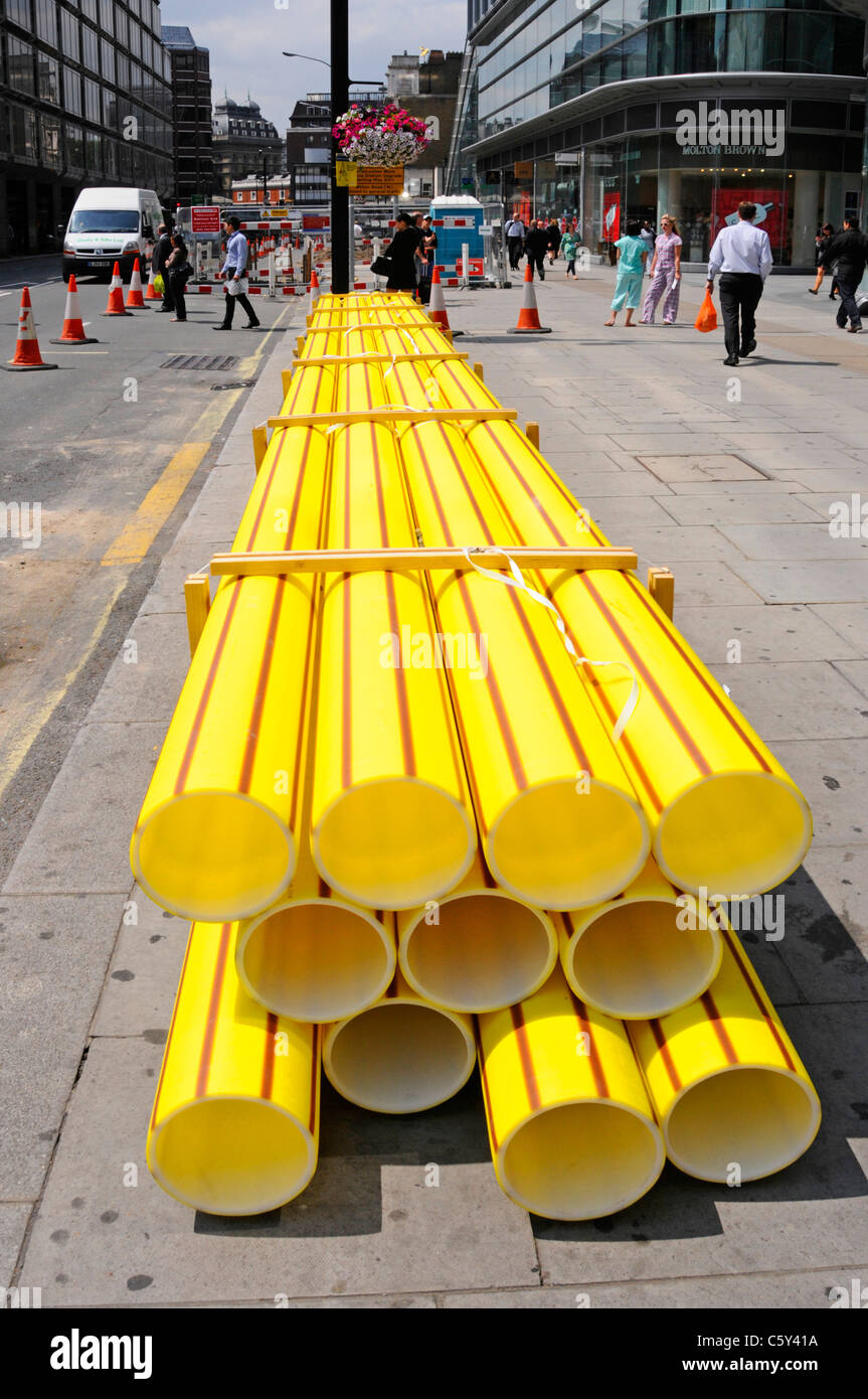 Infrastructure maintenance yellow plastic gas main pipes stacked on pavement to replace aging cast iron underground pipes Victoria London England UK Stock Photo