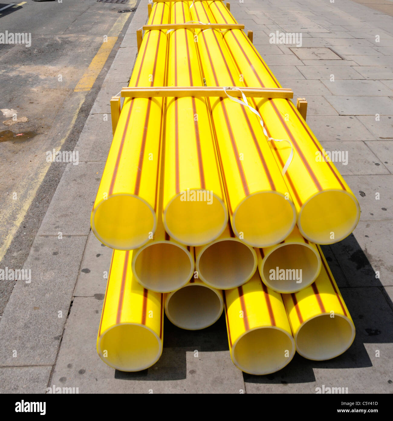 Infrastructure maintenance yellow plastic gas main pipe stacked on pavement to replace aging cast iron underground pipes Victoria London England UK Stock Photo