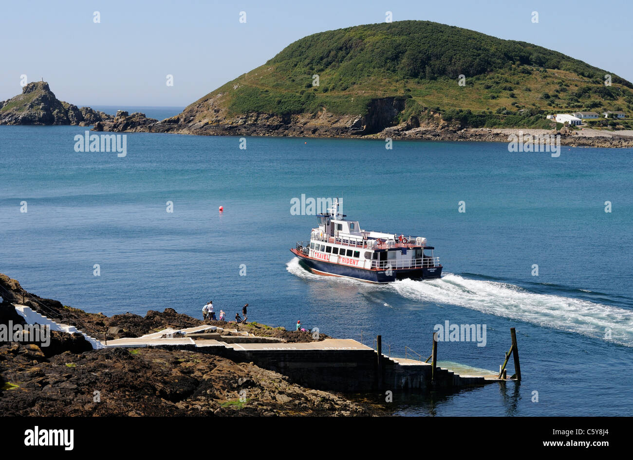 A Trident ferry leaves Rosaire steps  on Herm for St Peter Port in Guernsey. The island of Jethou can be seen in the background. Stock Photo