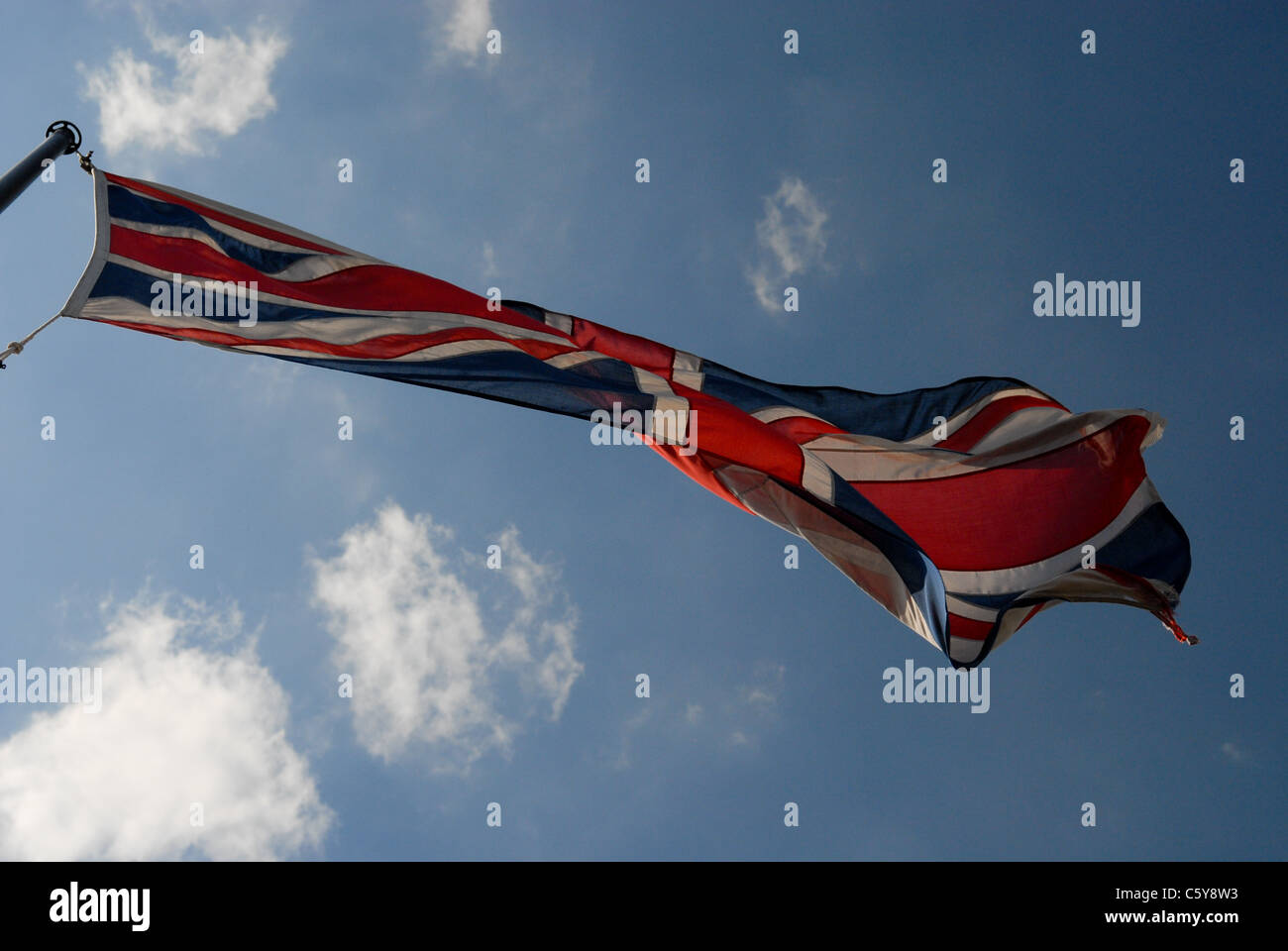 Battered Union Jack flag flying in the breeze against a deep blue sky ...