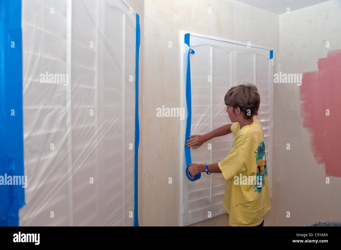 11 year years old caucasian boy using painter's tape to protect windows with plastic sheeting. MR © Myrleen Pearson Stock Photo