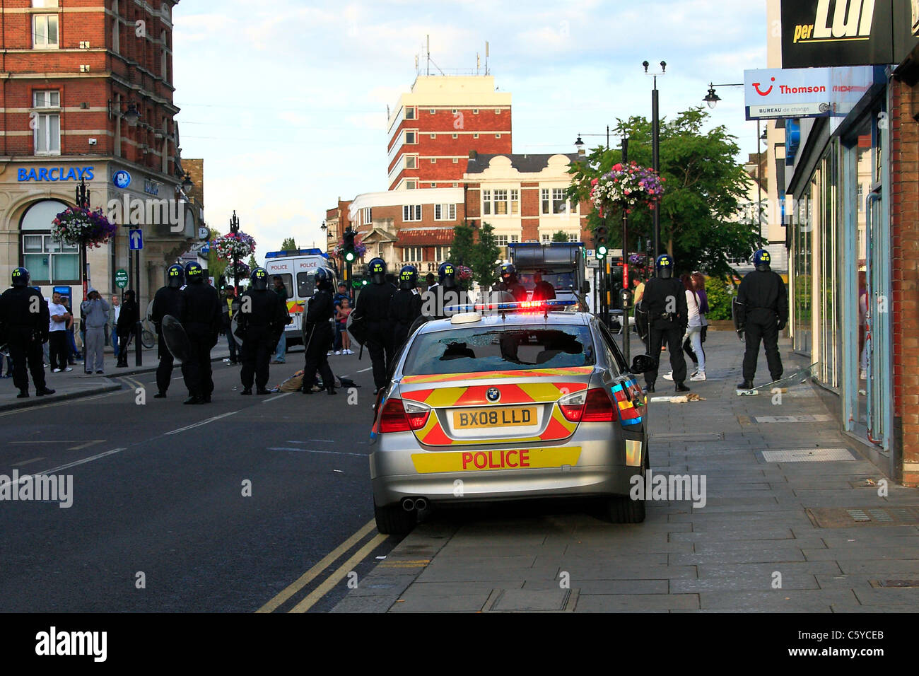 A BMW police car with all its windows smashed is guarded by a line of ...
