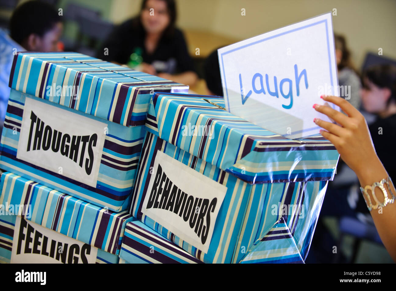 card saying laugh being put into boxes labeled thoughts behaviors feelings in a classroom Stock Photo