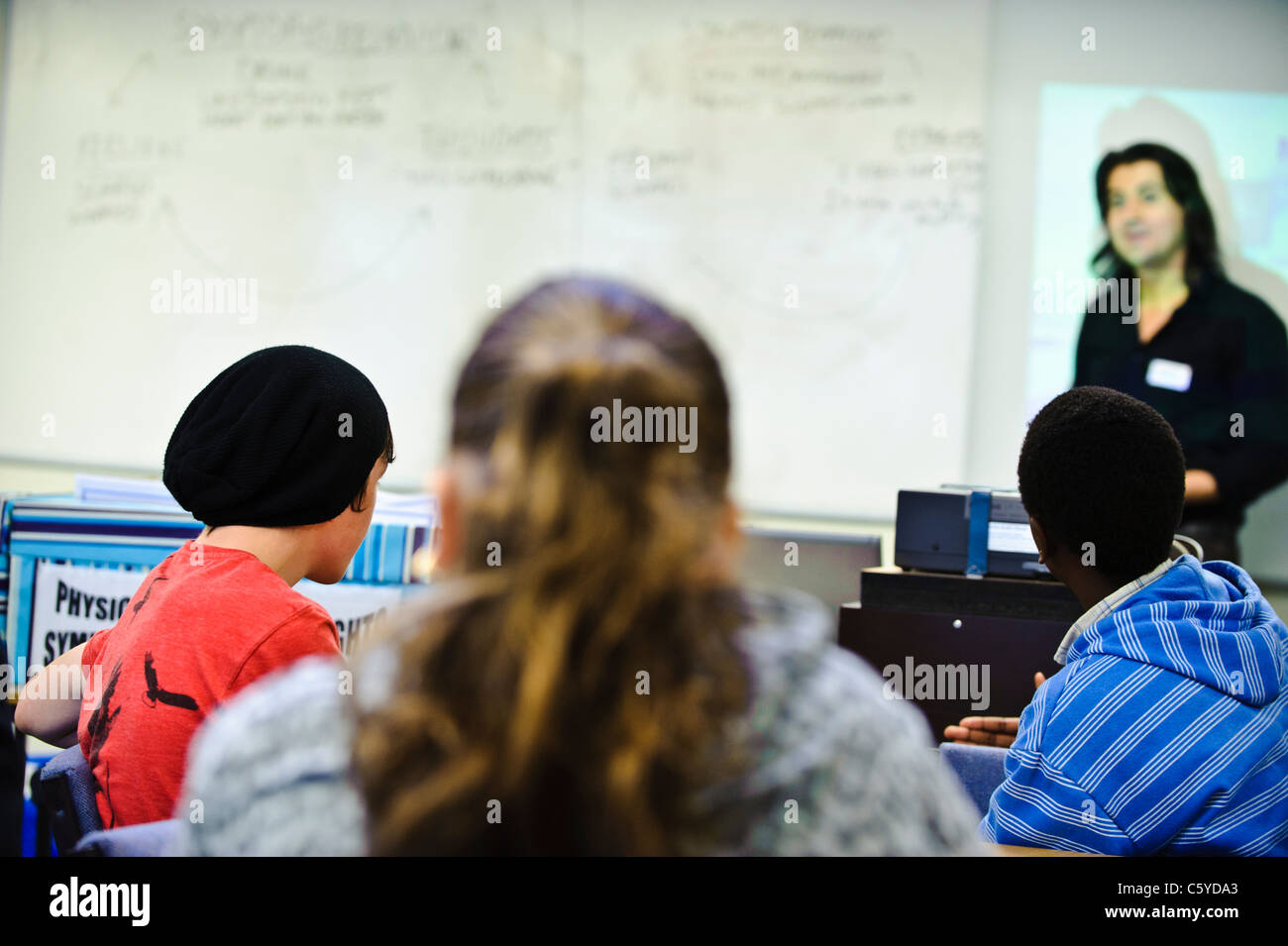 school children aged 12-13 years in classroom camera behind facing towards male teacher standing at the whiteboard Stock Photo