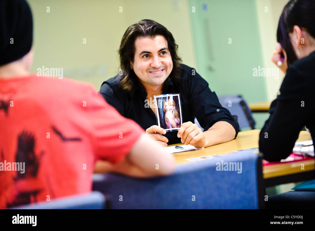 Adult male teacher in classroom setting holding up a photo of a celebrity towards two school children aged 12 to 13 years Stock Photo