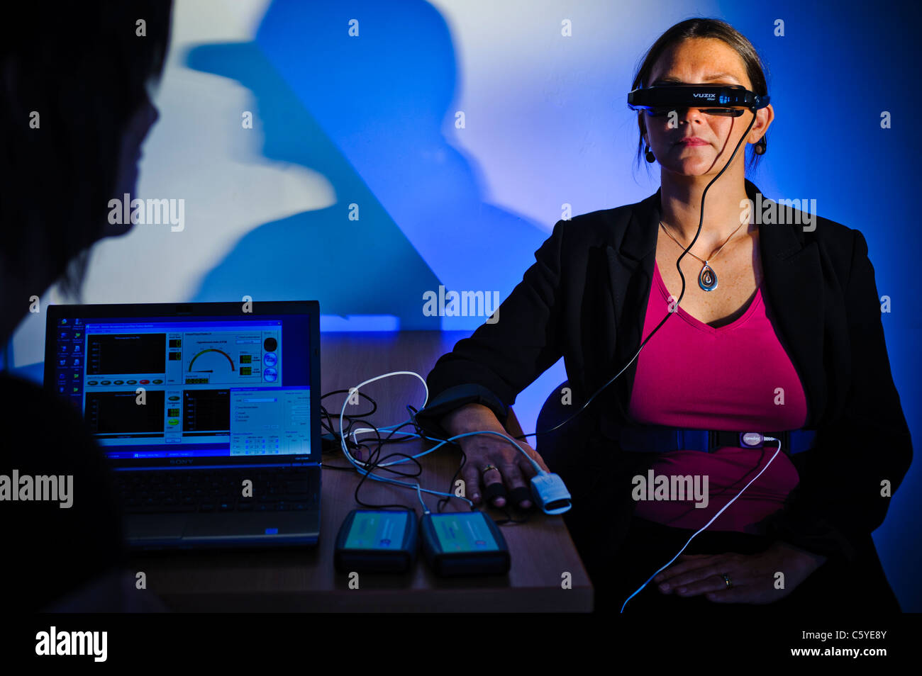 subject wearing virtual reality goggles in scientific study to treat phobia laptop showing results on screen in foreground blue Stock Photo